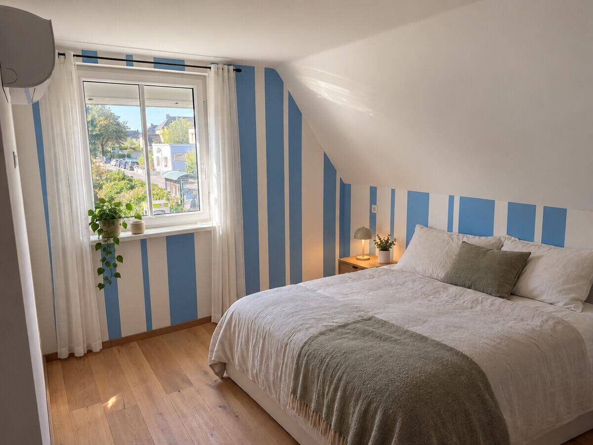 Gemütliches Schlafzimmer mit Holzboden, gestreifter Wand und Blick ins Grüne.