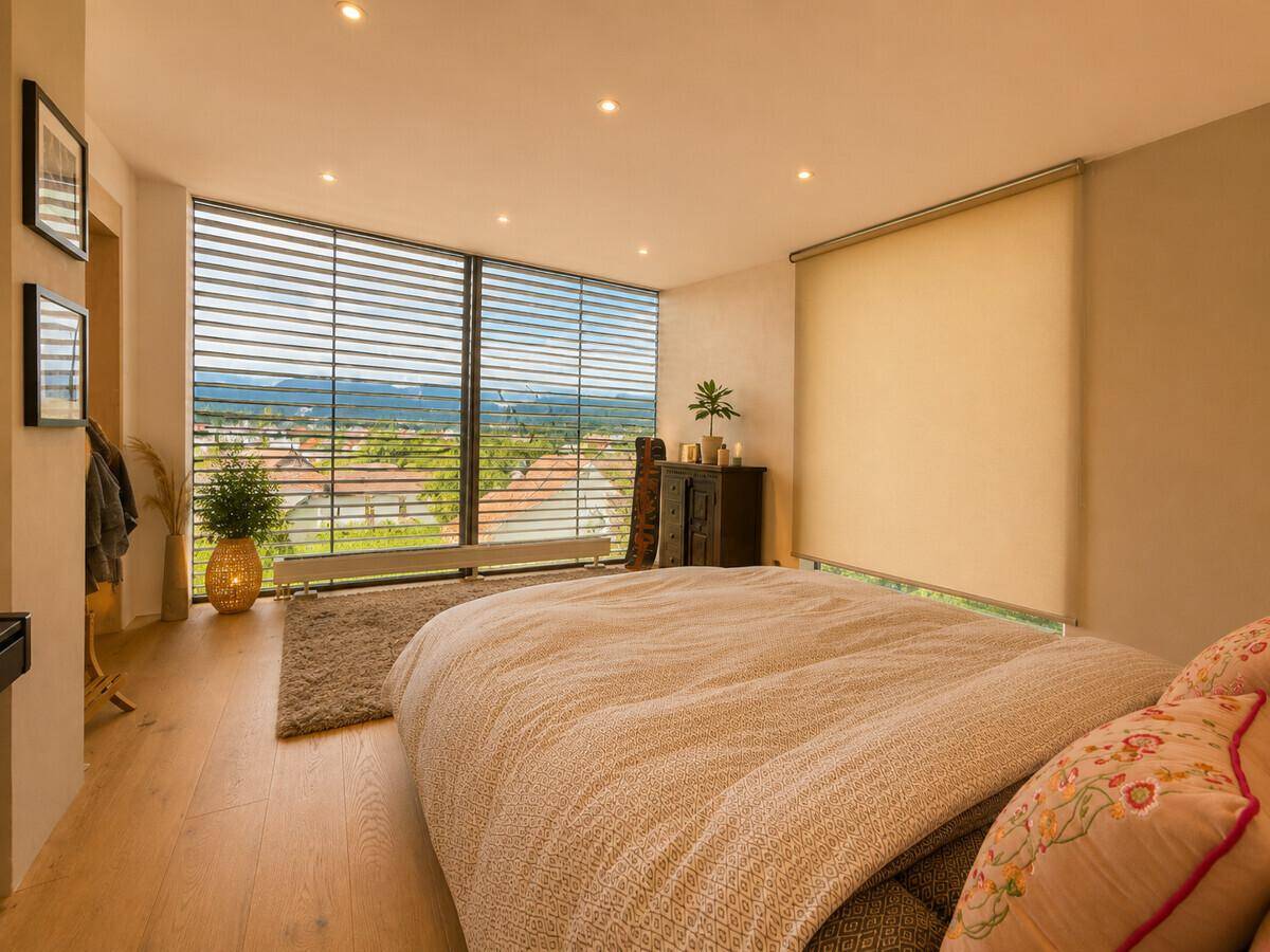 Helles Schlafzimmer mit großen Fenstern, Holzboden und weitem Blick über die Landschaft.