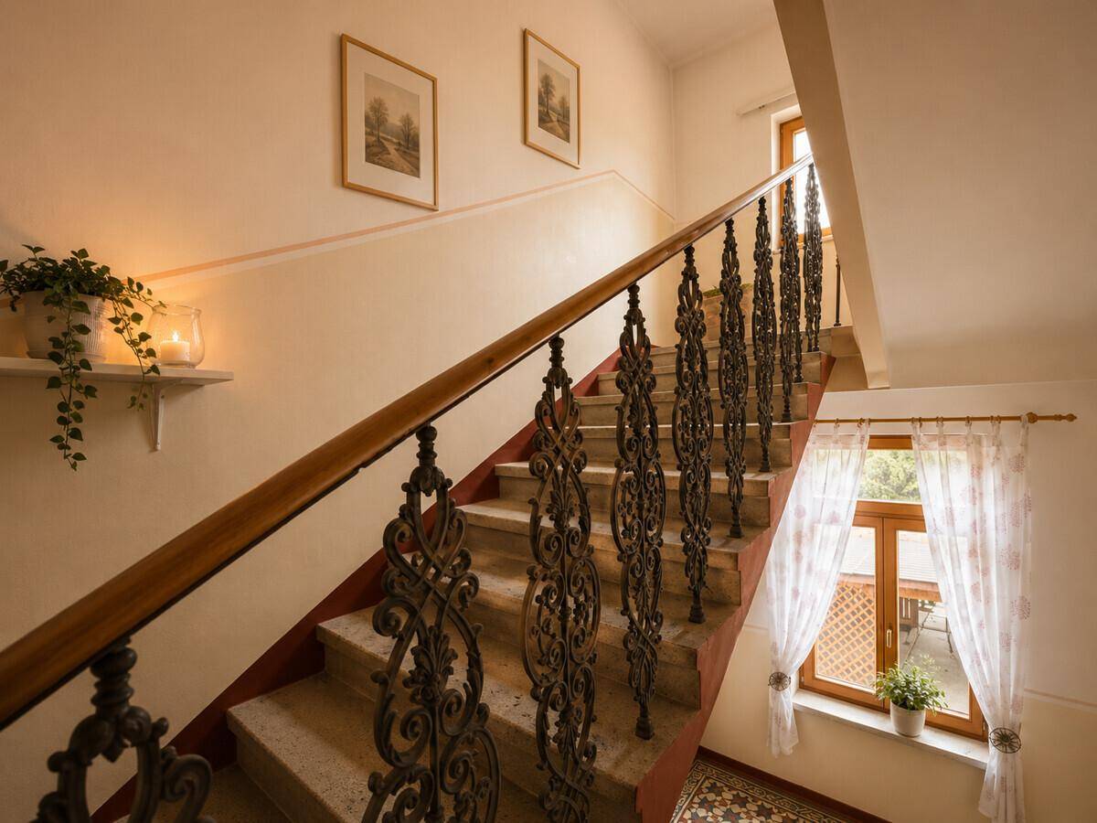 Elegante Treppe mit schmiedeeisernem Geländer und Fenster mit Vorhängen.