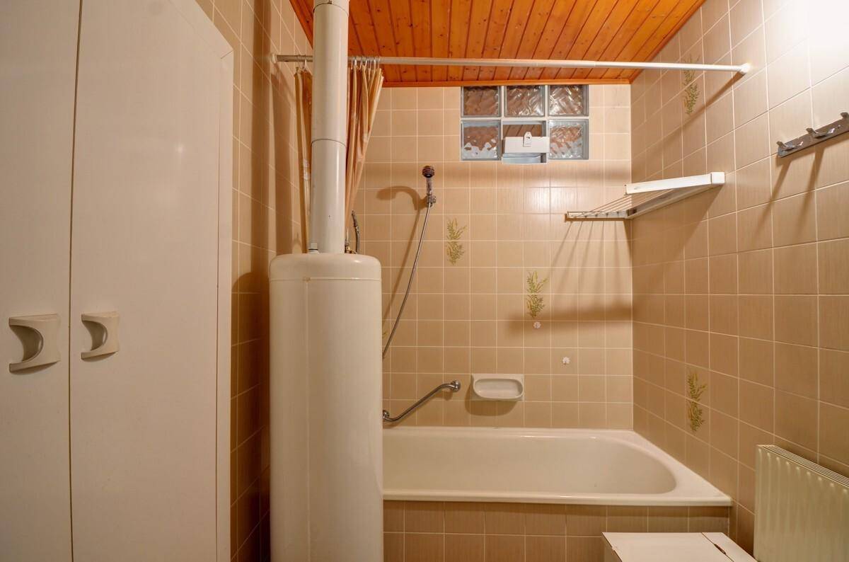 Badezimmer mit Badewanne, beigefarbenen Fliesen und Holzdecke im traditionellen Stil.