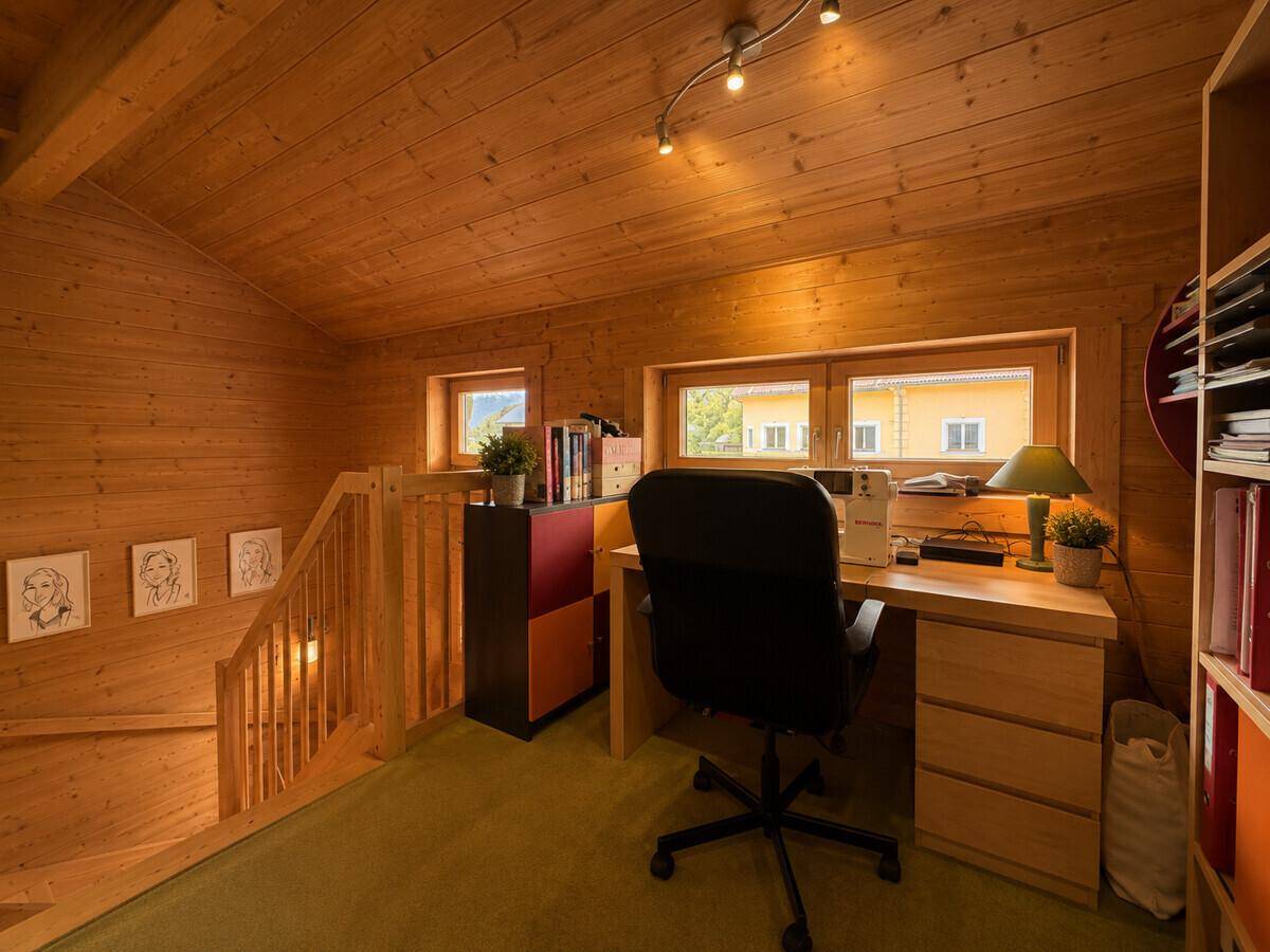 Helles Arbeitszimmer im Dachgeschoss mit Schreibtisch, Bücherregal und Holzwänden.