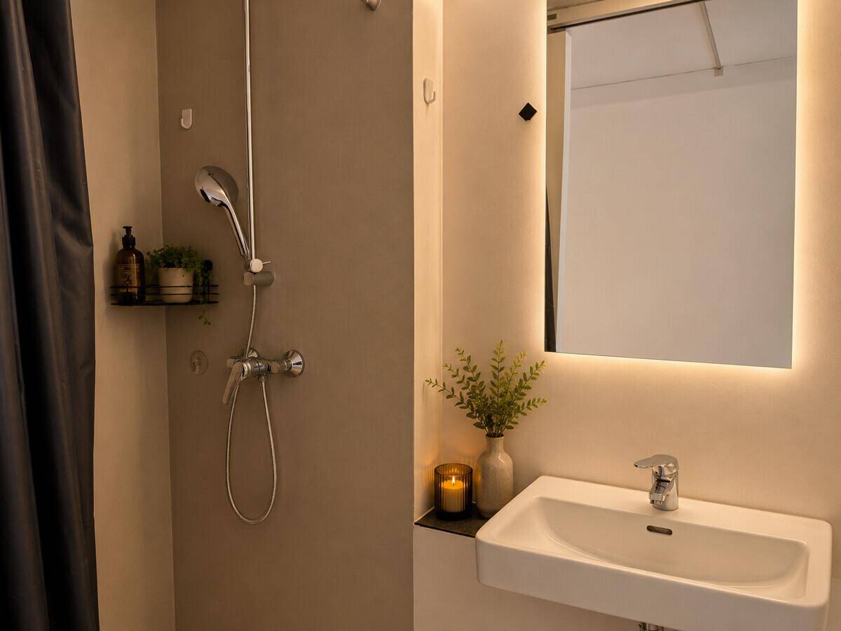 Modernes Badezimmer mit Duschbereich, Waschbecken und beleuchtetem Spiegel.