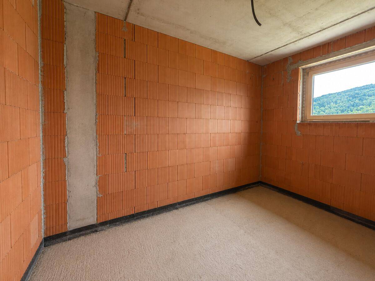 Schlafzimmer im Rohbau mit unverputzten Ziegelwänden und Fenster.