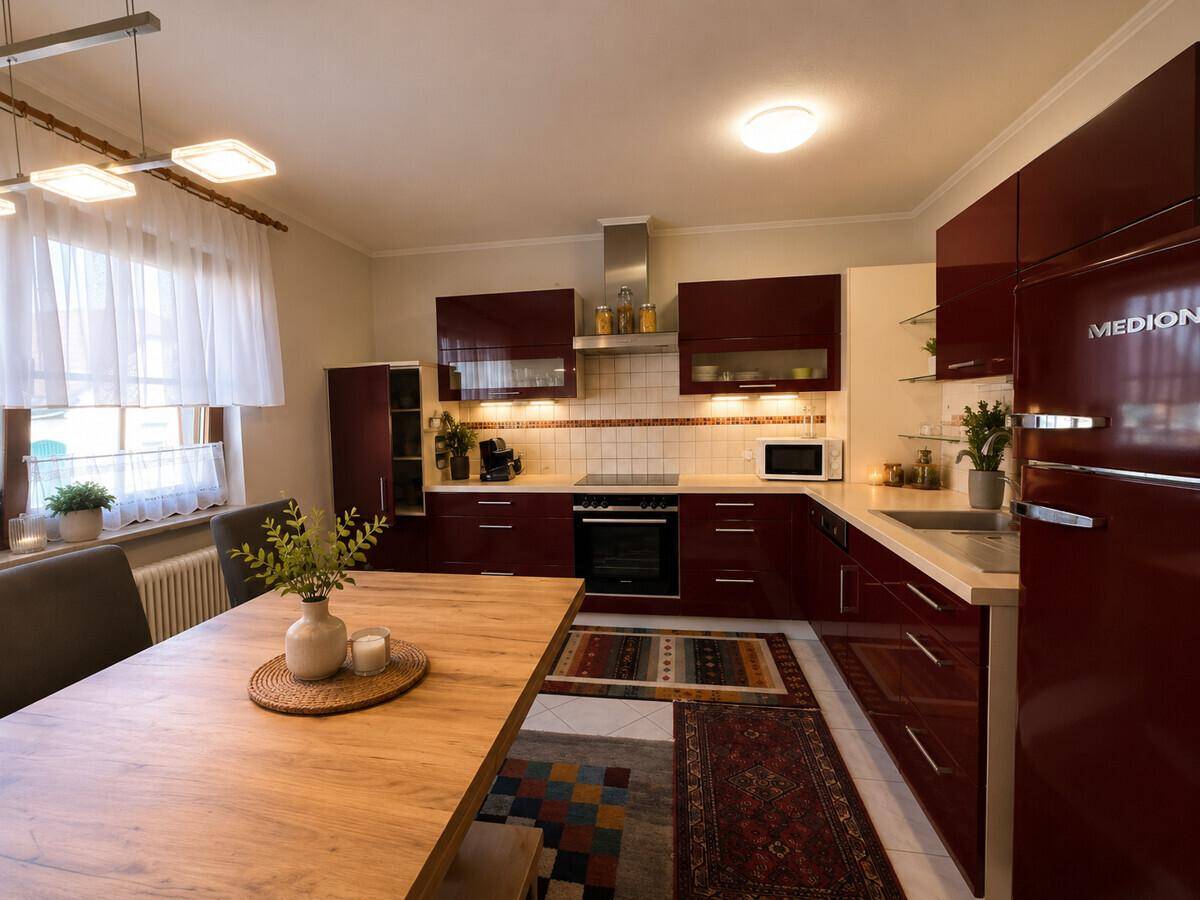Moderne Küche mit weinroten Hochglanzfronten, Esstisch und Teppichen.