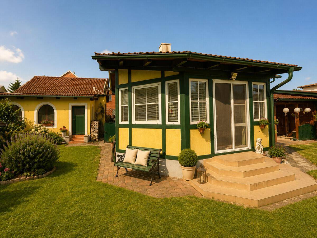 Angebauter Wintergarten mit gelb-grüner Fassade, Stufen und Gartenbank.