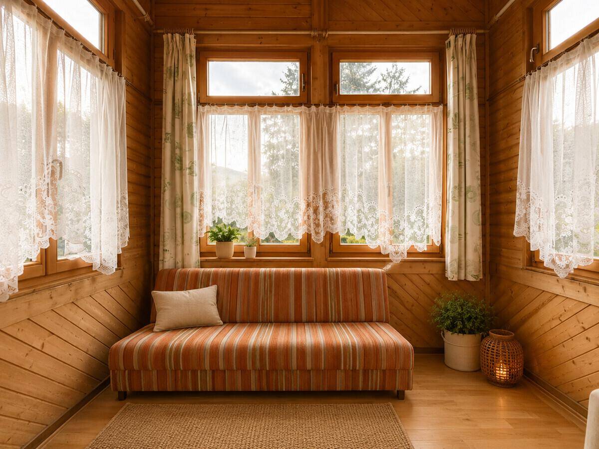 Gemütlicher Wintergarten mit Holzverkleidung, vielen Fenstern und gestreiftem Sofa.