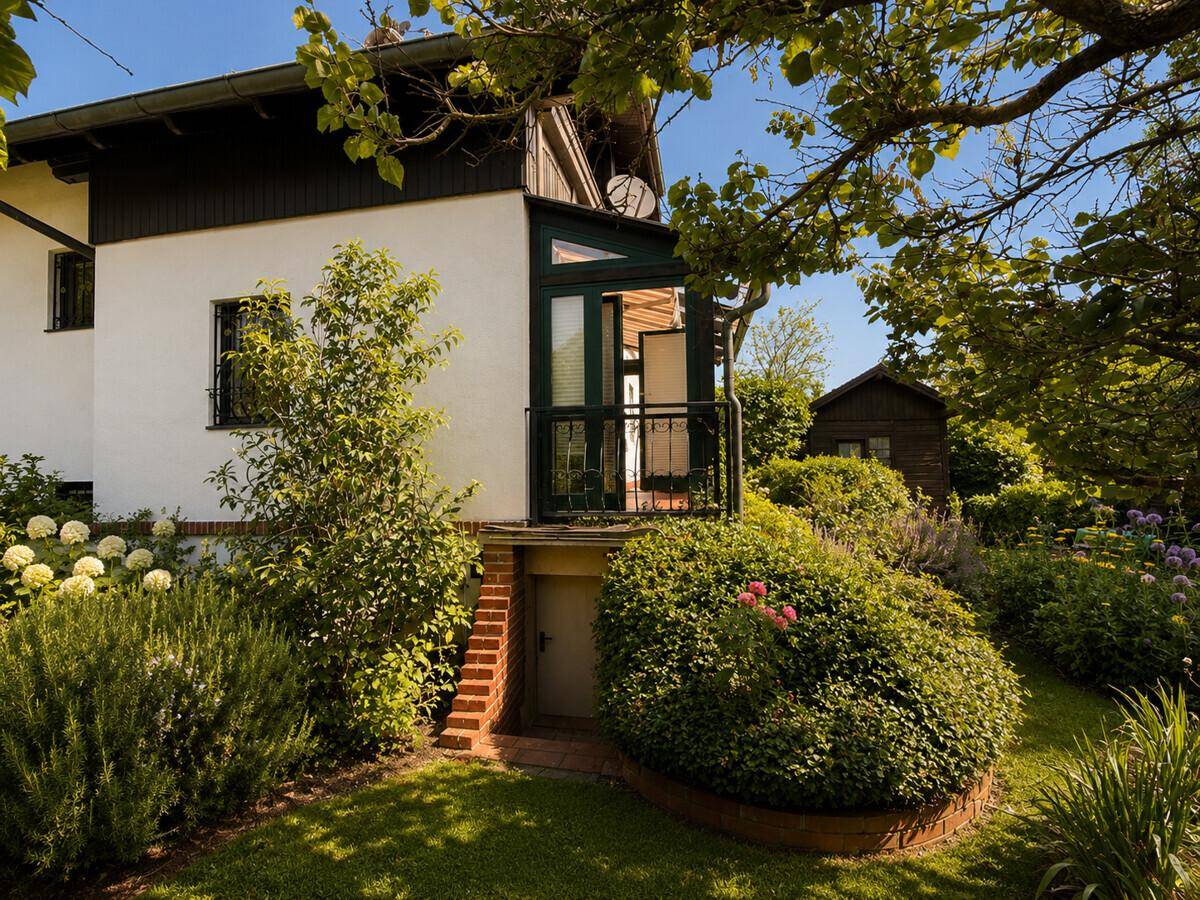 Hausfassade mit Zugang zum Garten und Keller, umgeben von gepflegter Bepflanzung.