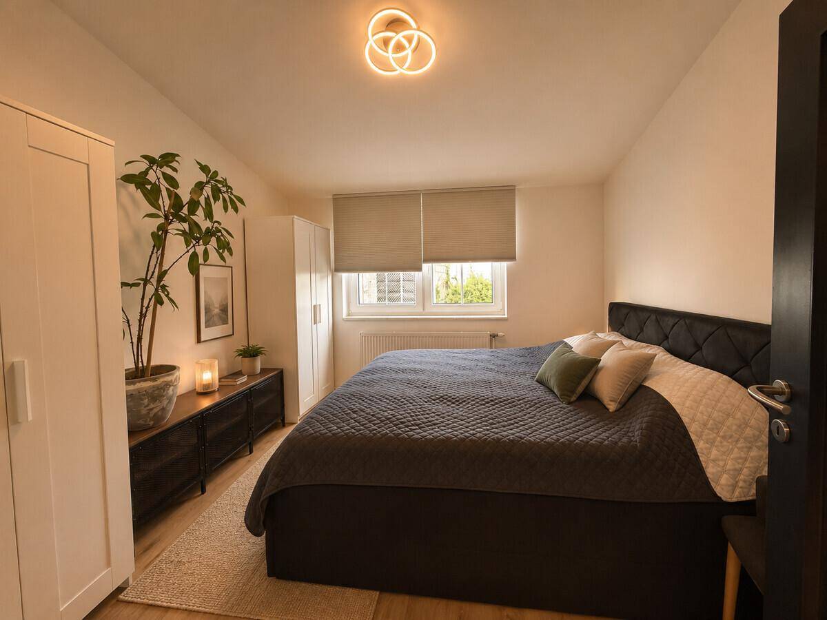 Gemütliches Schlafzimmer mit Doppelbett, weißem Kleiderschrank und einer Zimmerpflanze am Fenster.