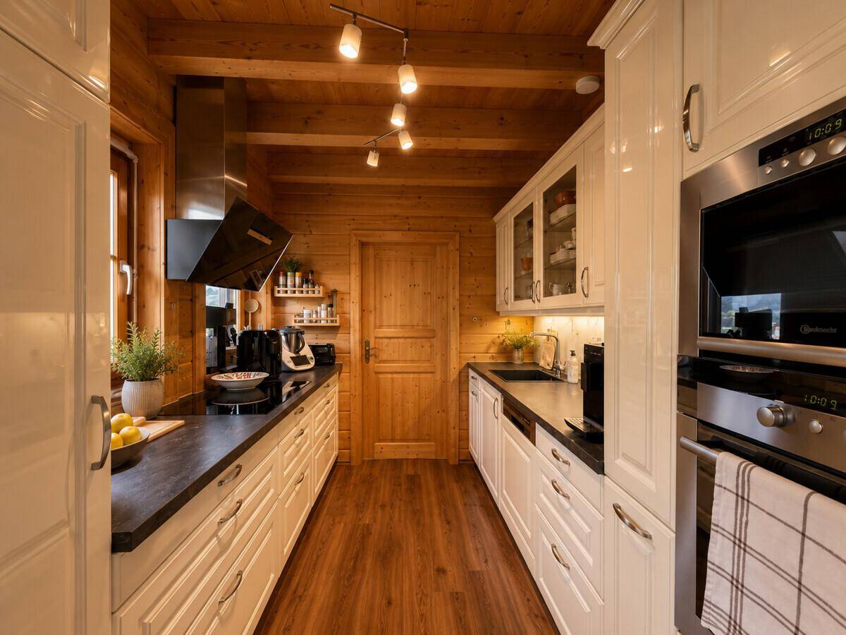Helle Holzküche mit weißen Schränken, modernen Geräten und Holzbalkendecke.