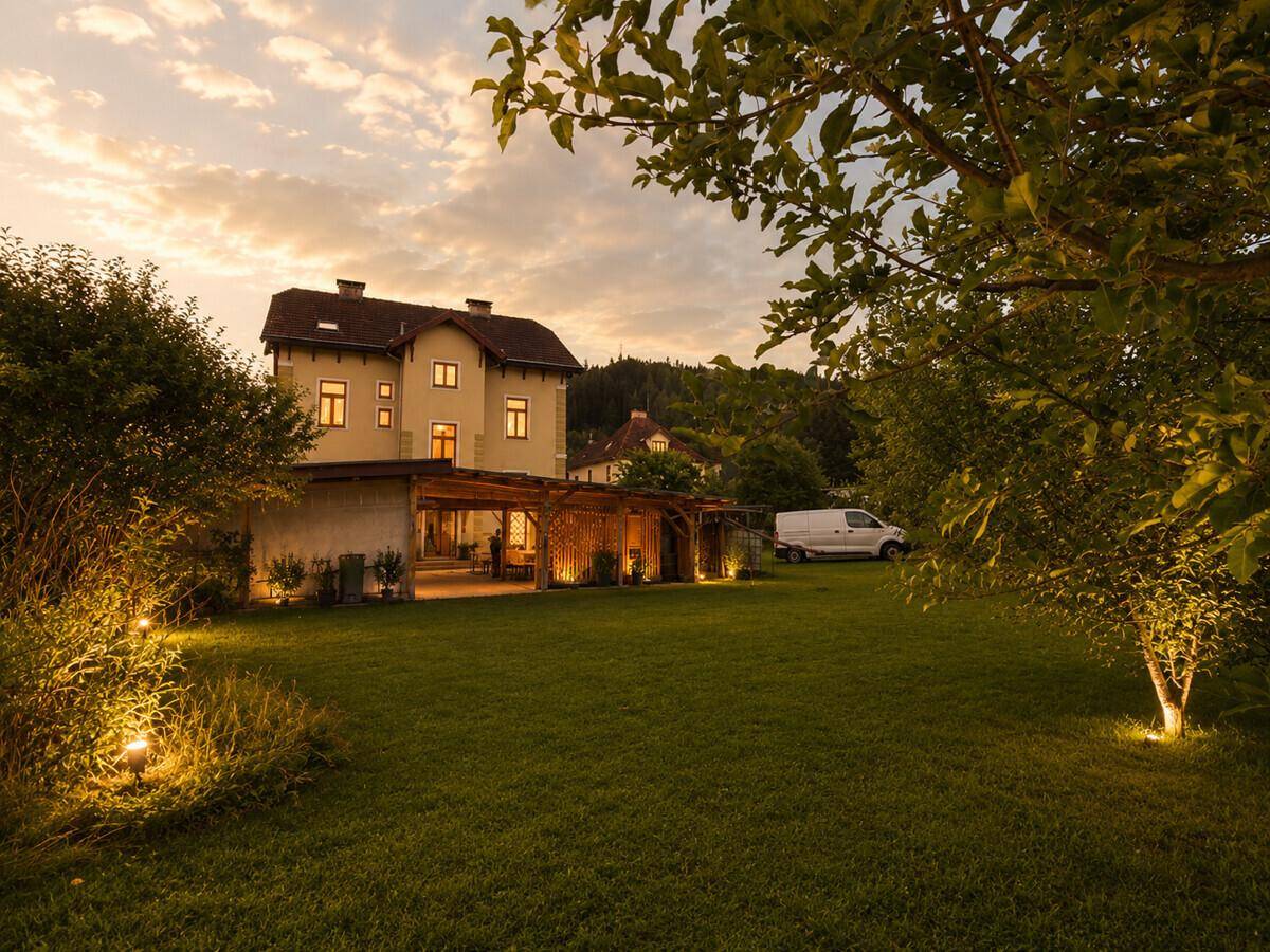 Großer Garten hinter dem Haus mit weitläufiger Rasenfläche und beleuchtetem Unterstand bei Sonnenuntergang.