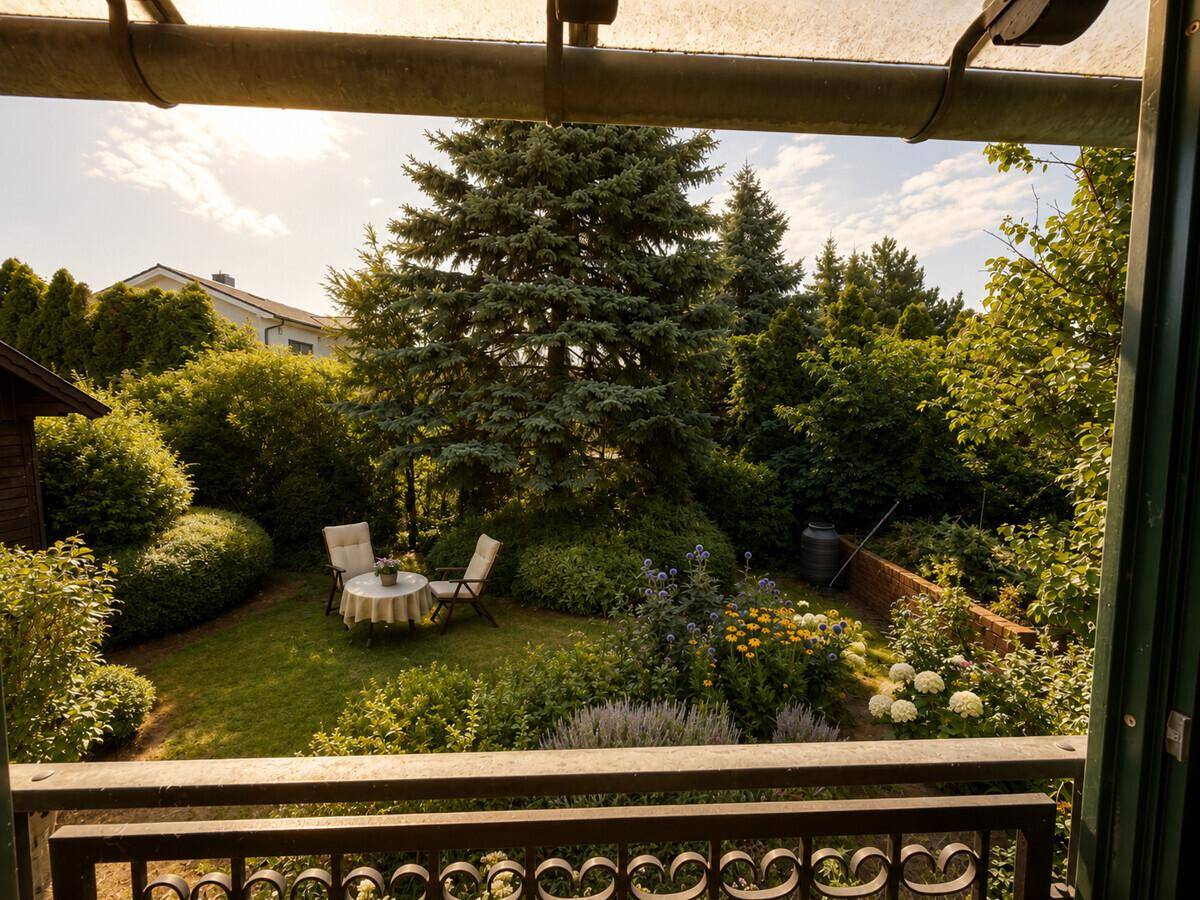 Blick vom Balkon auf den idyllischen Garten mit üppiger Vegetation und kleiner Sitzecke.