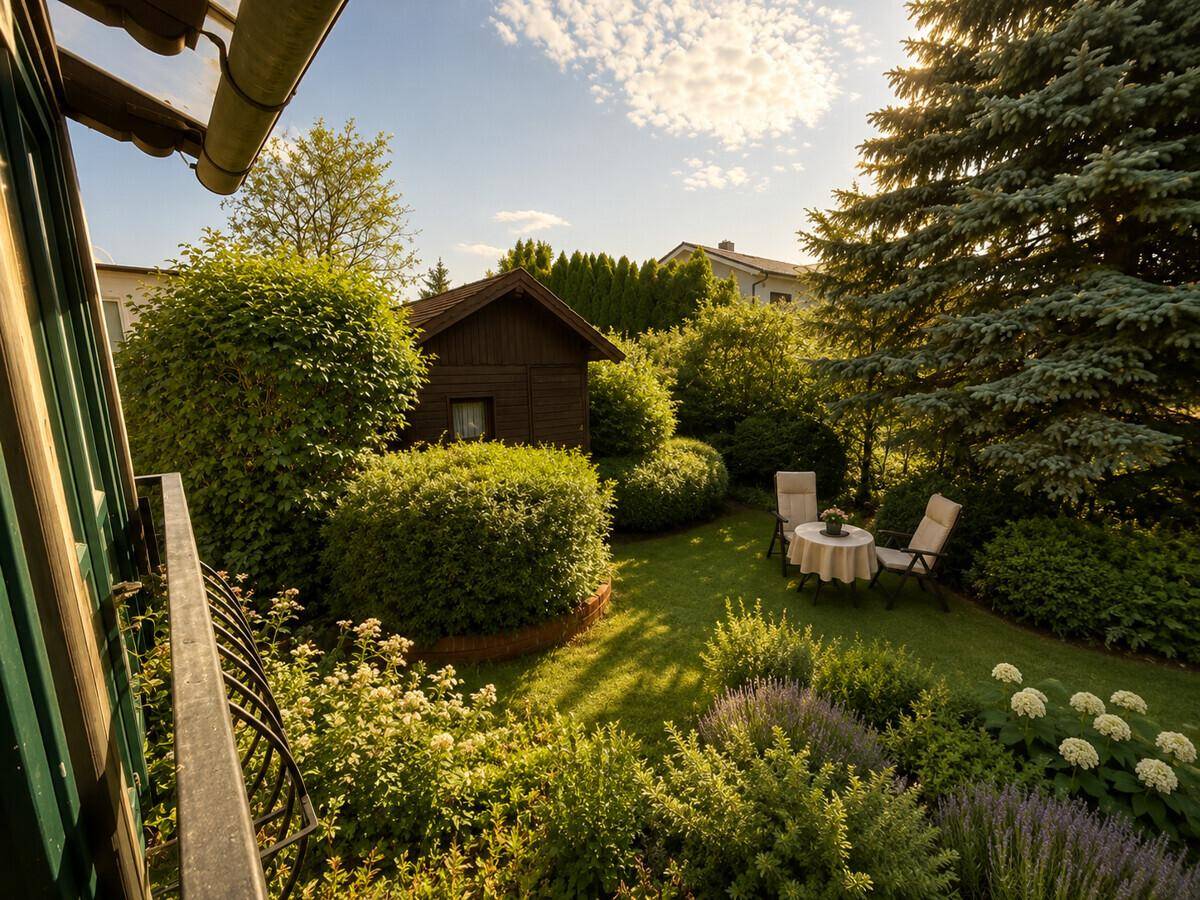 Panoramablick vom Balkon auf den weitläufigen Garten mit Rasen und Bäumen.