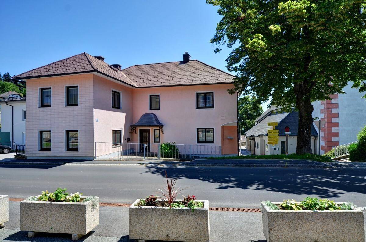 Frontansicht des rosa verputzten Hauses mit Satteldach und Blumenkübeln im Vordergrund.