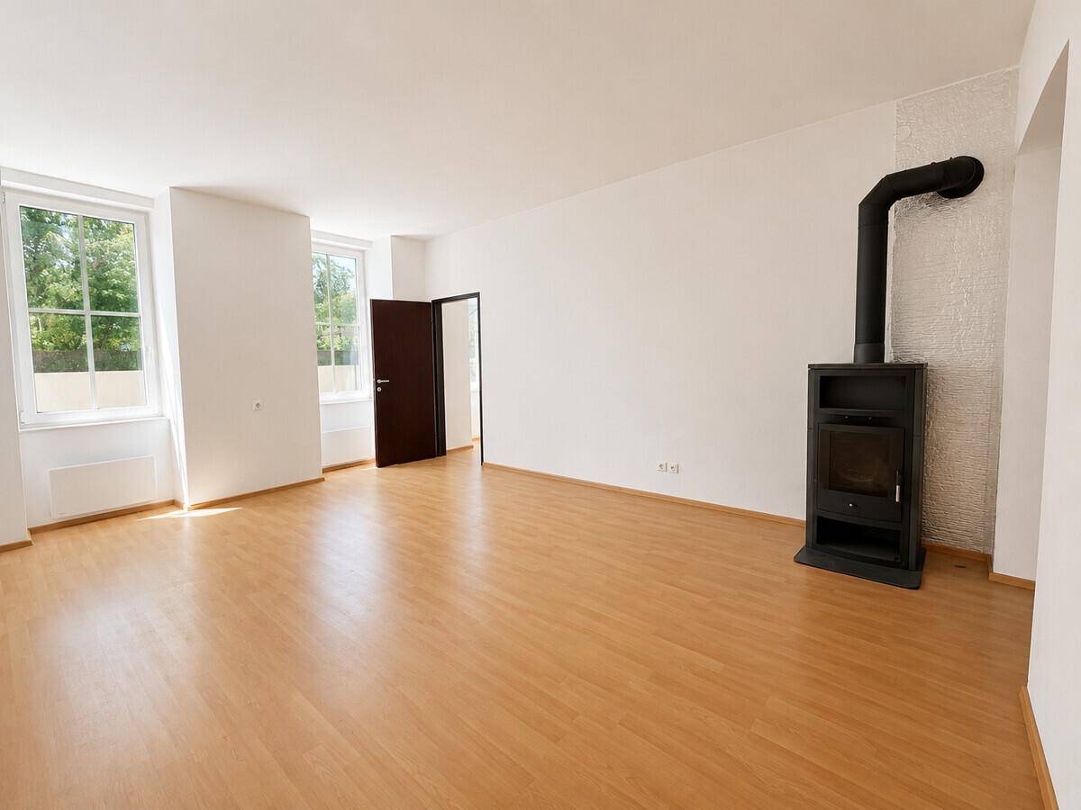 Geräumiges Wohnzimmer mit Laminatboden und einem modernen Holzofen als Wärmequelle.