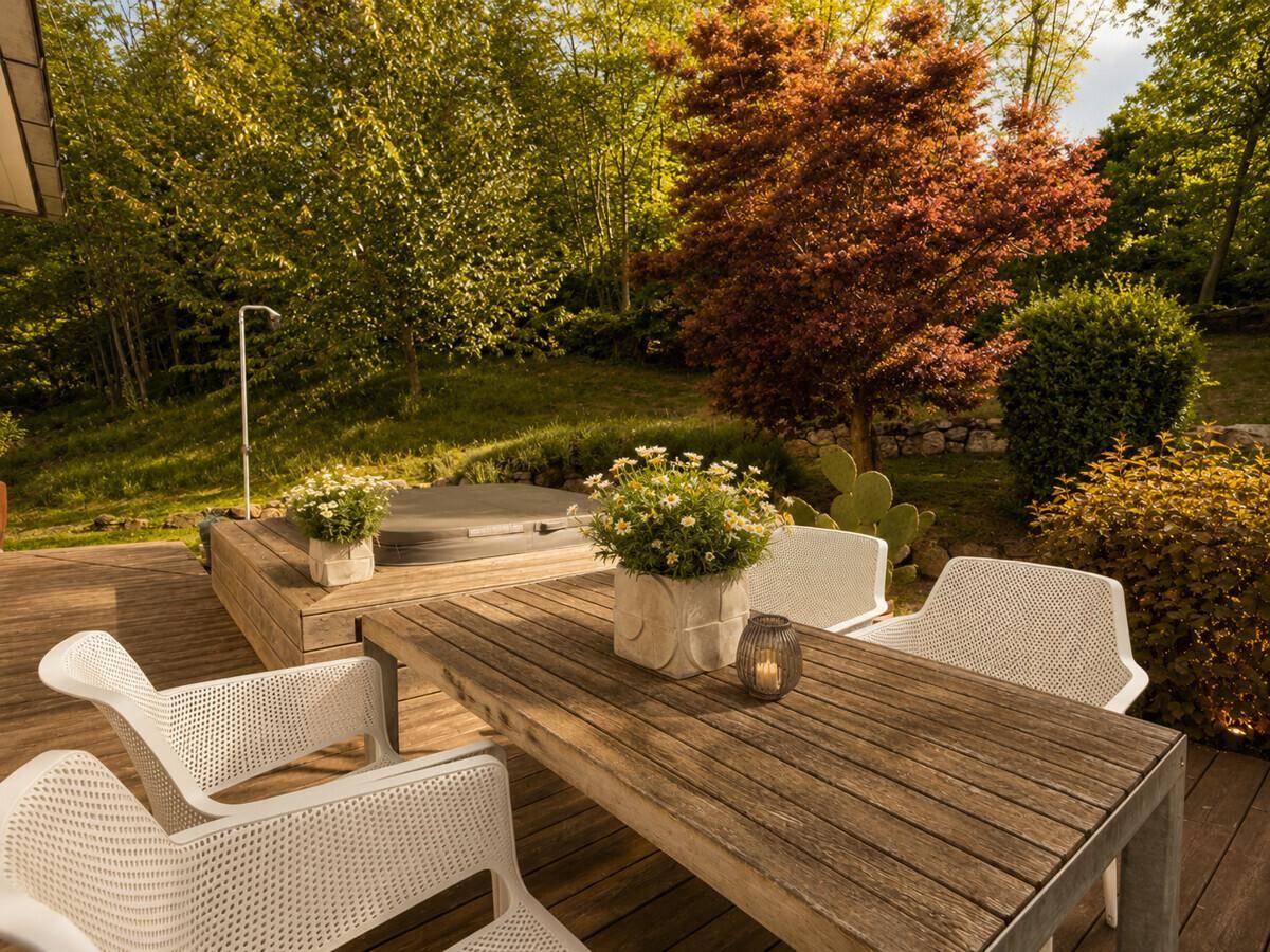 Holzterrasse mit Esstisch, Stühlen und integriertem Whirlpool im grünen Garten.