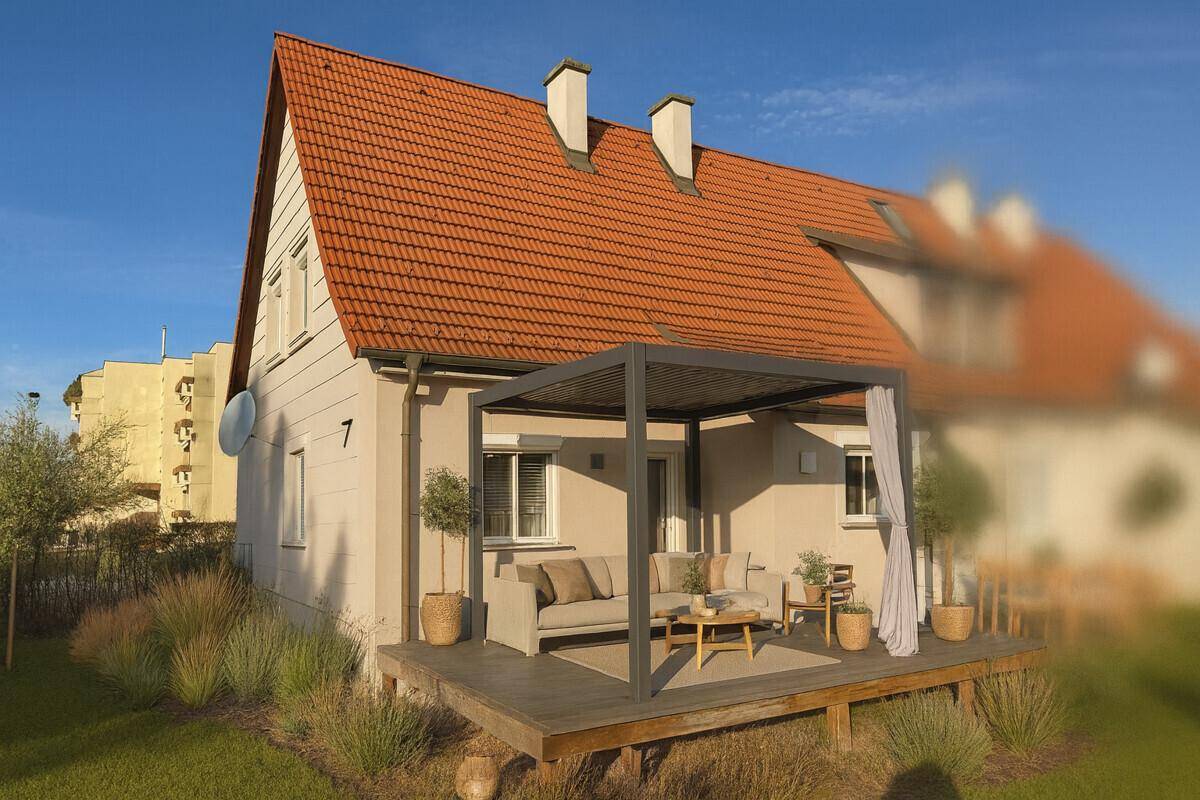 Modernes Einfamilienhaus mit großer Holzterrasse, Pergola und Gartenmöbeln.