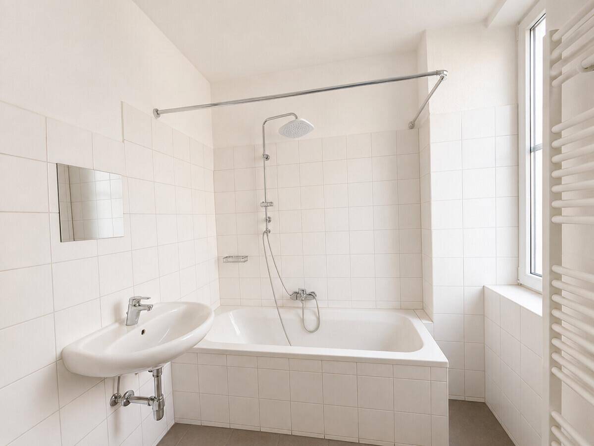 Helles Badezimmer mit weißen Fliesen, Badewanne mit Duschfunktion und Handtuchheizkörper.