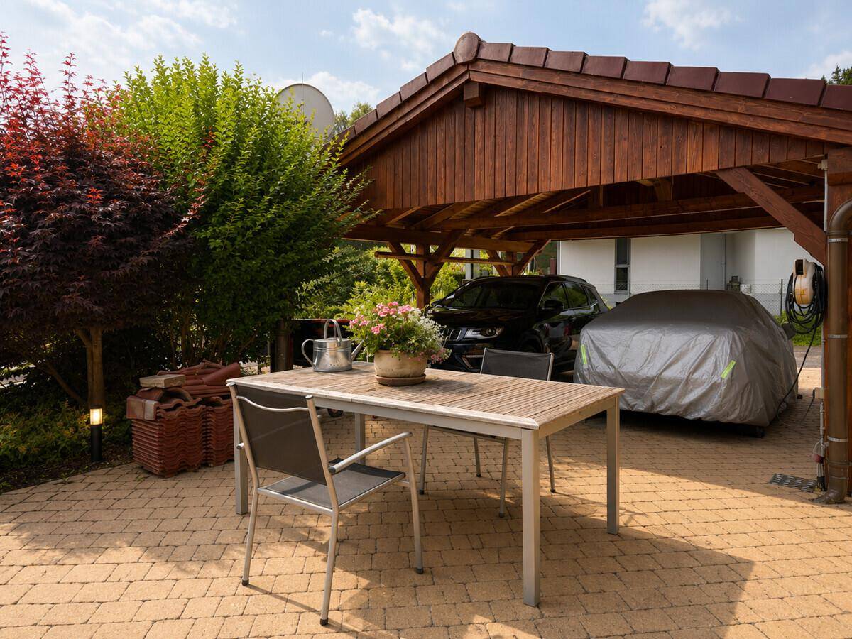 Überdachter Carport mit Stellplätzen und kleiner Terrasse für Mahlzeiten im Freien.