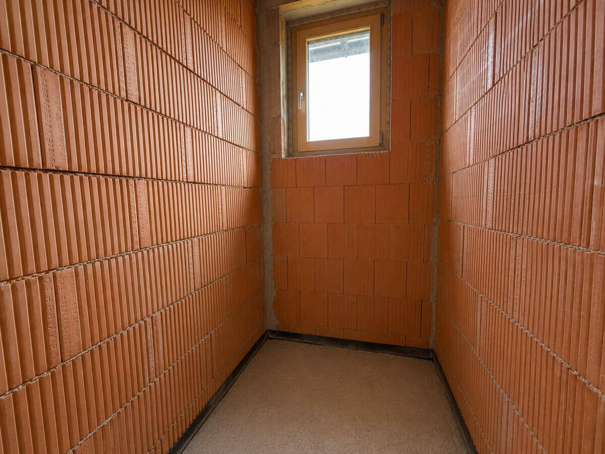 Kleiner Raum im Rohbau mit Ziegelwänden und einem Fenster.