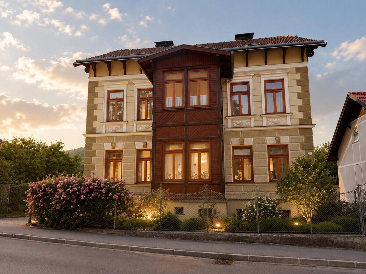 Historische Fassade des Gebäudes mit Erker und gepflegtem Vorgarten bei Abendlicht.