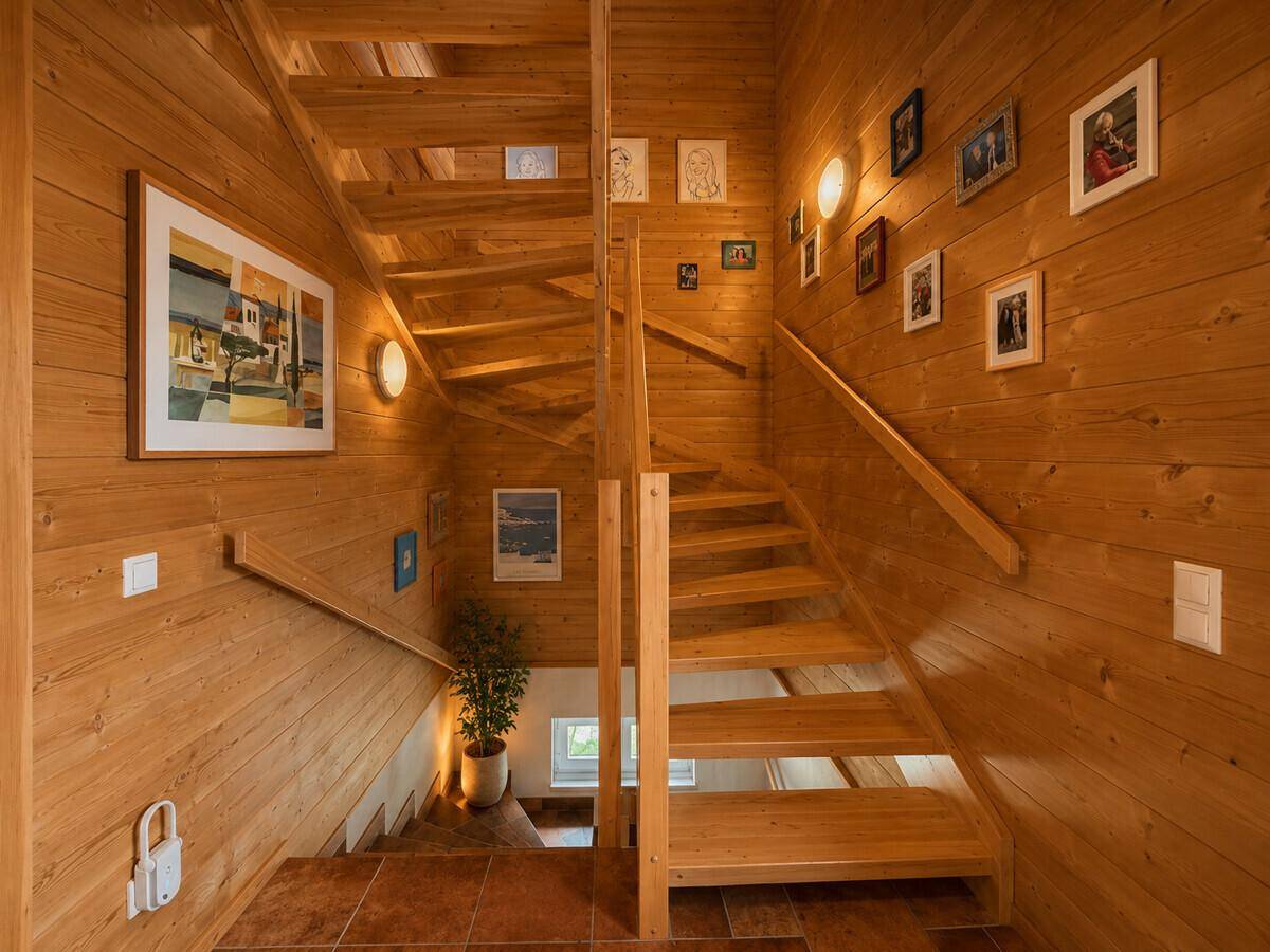 Helles Treppenhaus mit Holzstufen und Holzverkleidung, geschmückt mit Bildern.