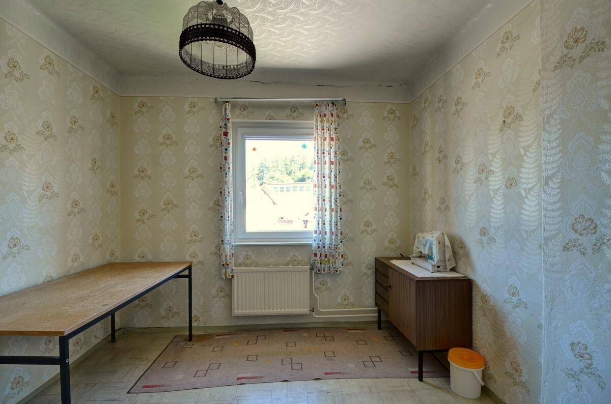 Zimmer mit großem Tisch, Kommode und Fenster mit Blick ins Grüne.