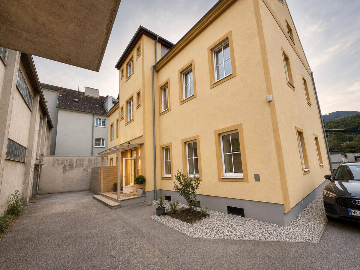 Rückansicht des Gebäudes mit Parkplatz und Zufahrt, umgeben von weiterer Bebauung.
