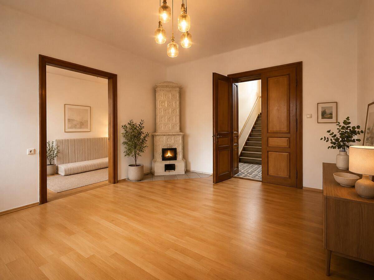 Helles Wohnzimmer mit Kachelofen, Holzboden und Zugang zu weiteren Räumen.
