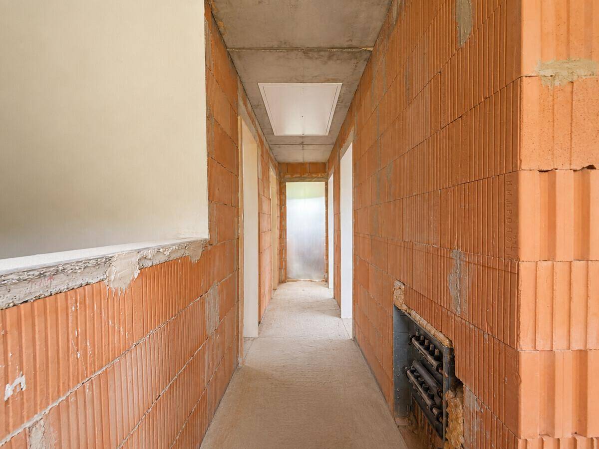 Flur im Rohbau mit unverputzten Ziegelwänden und Betonboden.