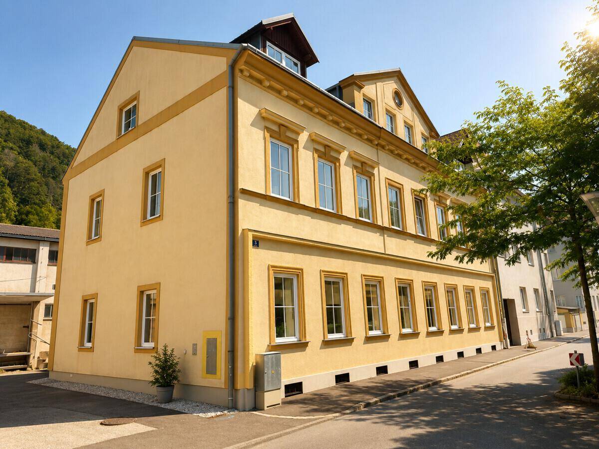 Seitenansicht des historischen Gebäudes mit gelber Fassade und Blick auf die umliegende Natur.