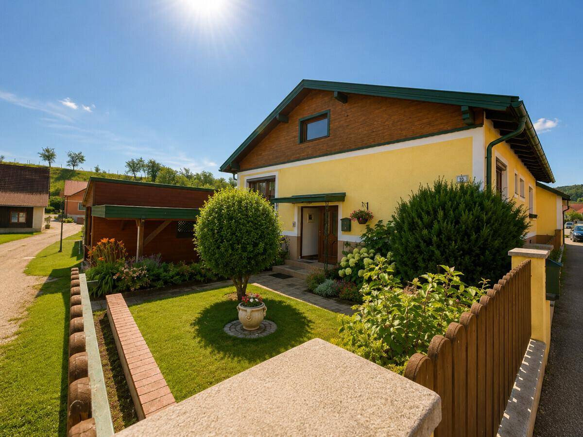 Gelbes Einfamilienhaus mit Vorgarten, Holzzaun und gepflegter Bepflanzung.