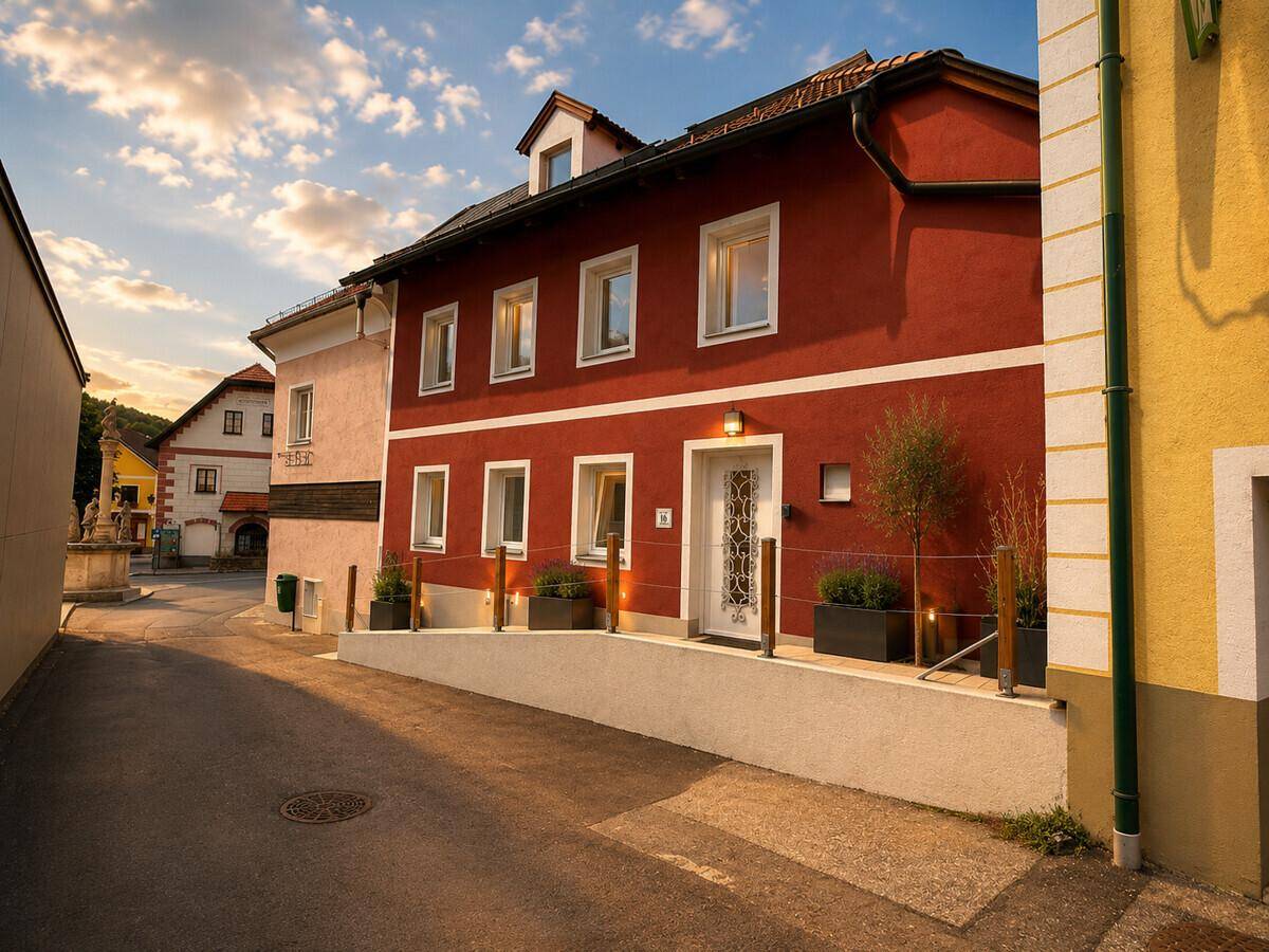 Rotes Gebäude in einer Gasse mit gepflastertem Gehweg und umliegenden Häusern.