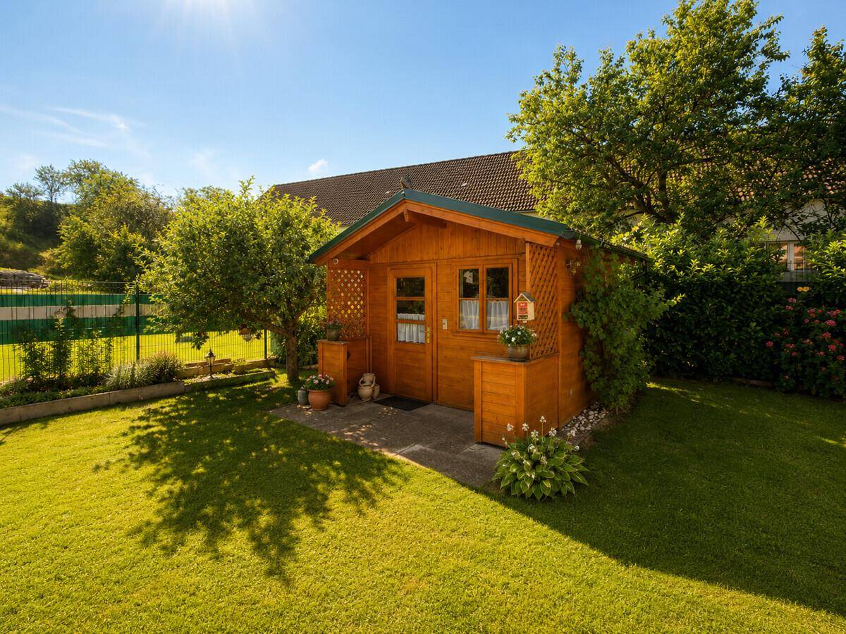Kleines Gartenhaus aus Holz mit Fenstern, Blumenkästen und gepflegtem Rasen.