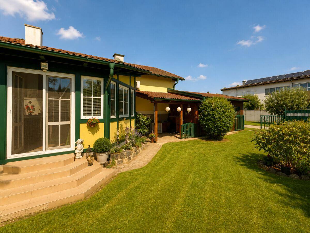 Gepflegter Garten mit Rasenfläche, Stufen zum Wintergarten und Solarpaneelen im Hintergrund.