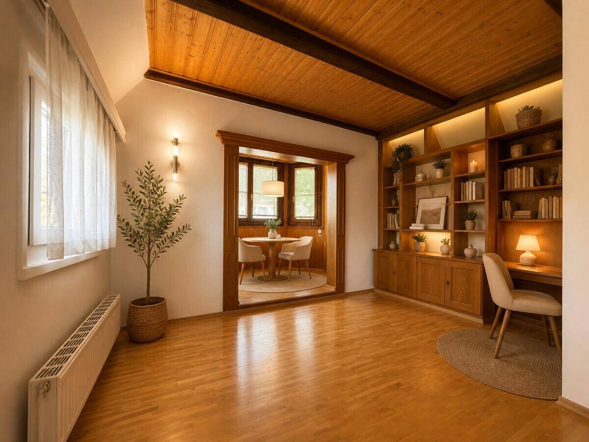 Geräumiges Wohnzimmer mit Holzboden, Bücherregal und Zugang zu einem Essbereich.