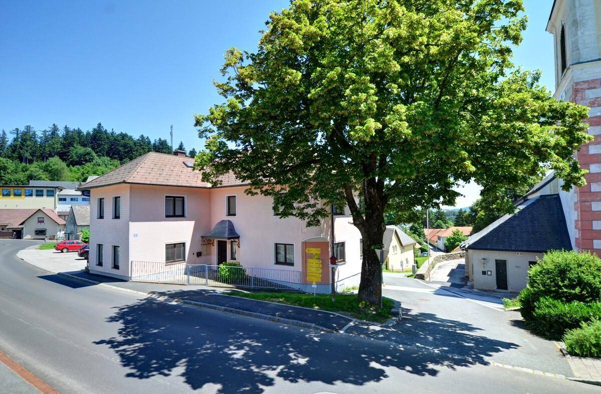 Das rosa verputzte Haus mit Satteldach und großem Baum im Vordergrund an einem sonnigen Tag.