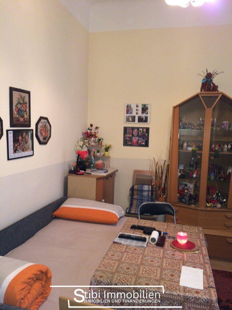 Gemütliches Schlafzimmer mit Bett, Tisch und einer Vitrine, dekoriert mit persönlichen Gegenständen und Bildern.