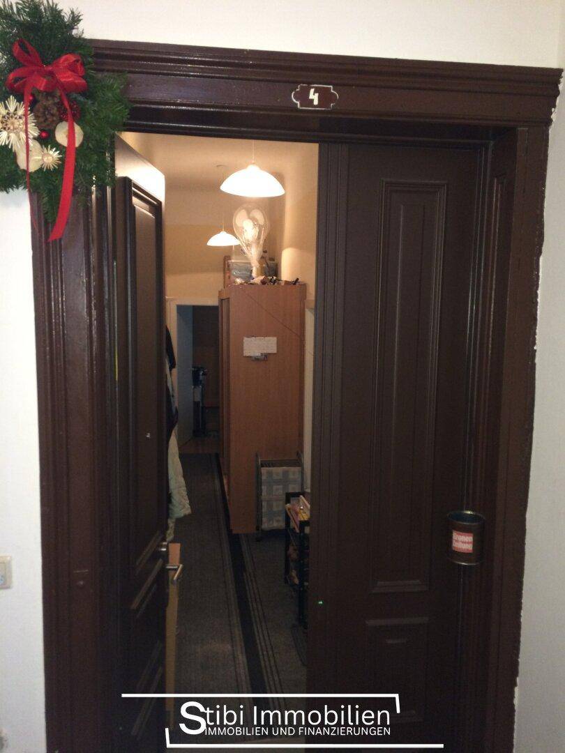 Blick durch eine offene dunkle Holztür in einen schmalen Flur mit Weihnachtsdekoration am Türrahmen.