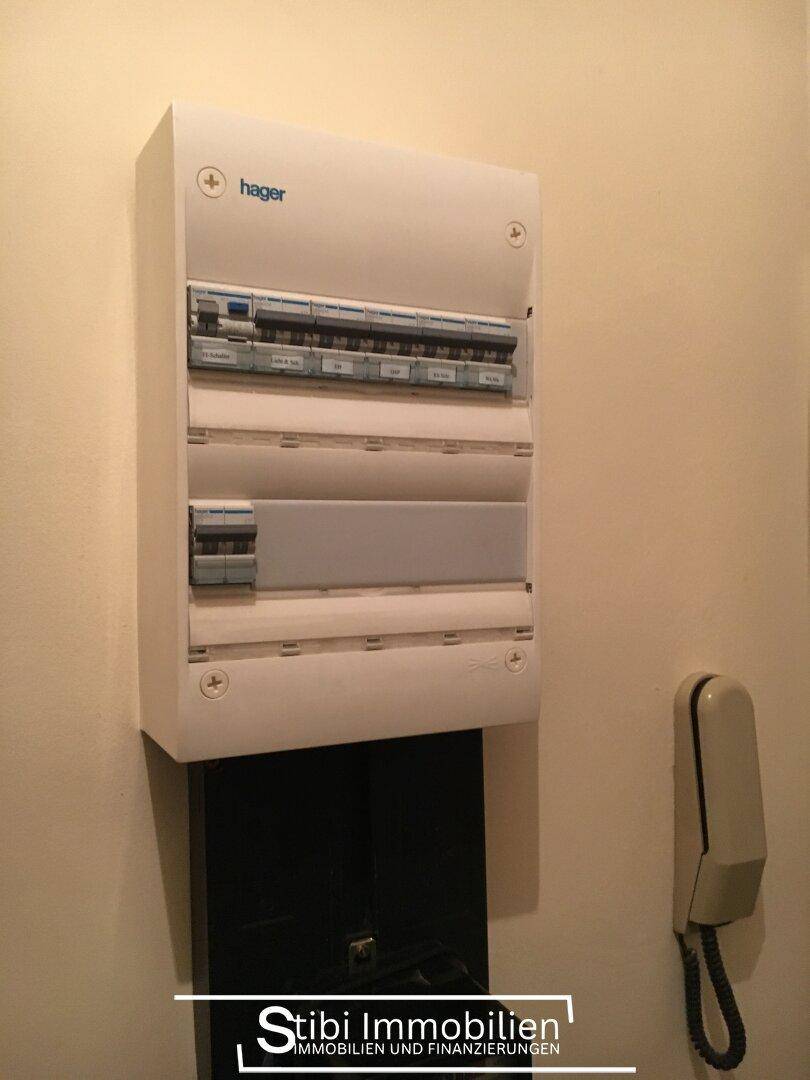 Elektrischer Sicherungskasten der Marke Hager und eine Gegensprechanlage an einer hellen Wand.