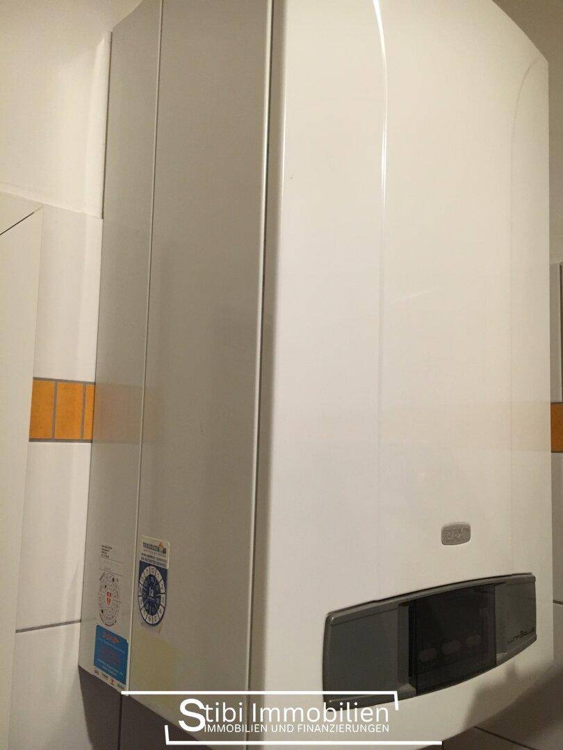 Weißer Gasboiler oder Warmwasserbereiter an einer gefliesten Wand, möglicherweise in einem Hauswirtschaftsraum.
