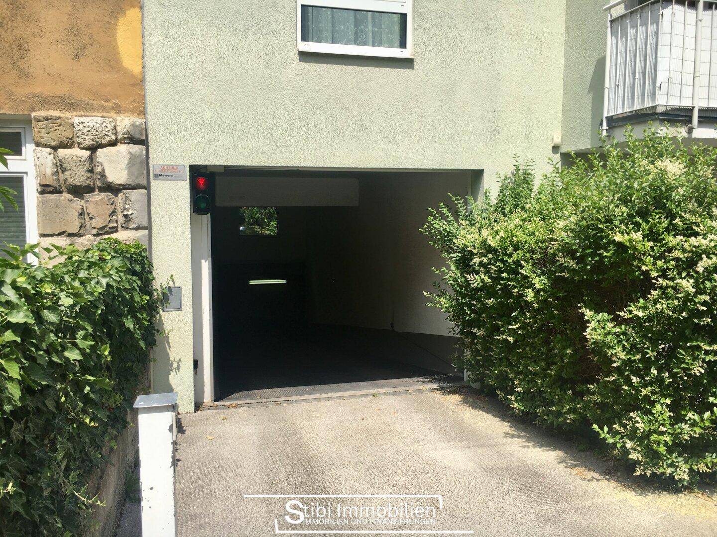 Einfahrt zur Tiefgarage mit Ampelsystem, umgeben von grünen Hecken und einer modernen Fassade.