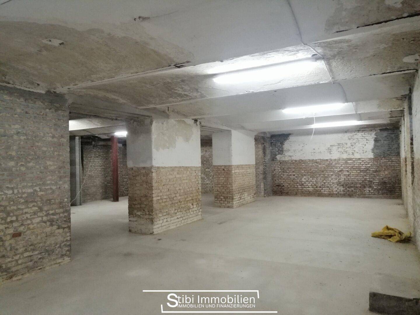 Geräumiger Kellerraum mit unverputzten Ziegelwänden, Betonpfeilern und Deckenbeleuchtung.