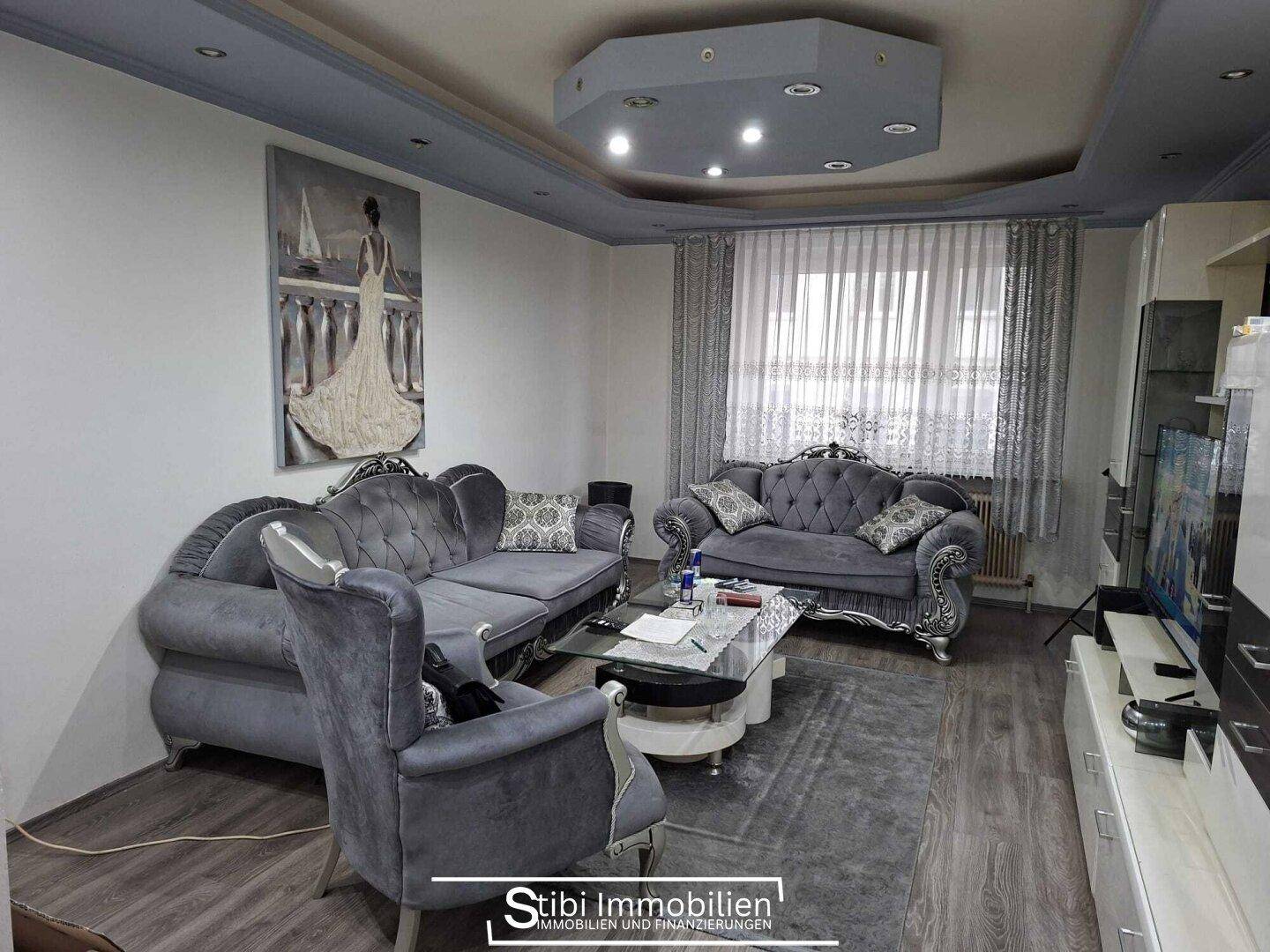 Geräumiges Wohnzimmer mit grauen Sofas, Couchtisch und modernem Deckenlicht.