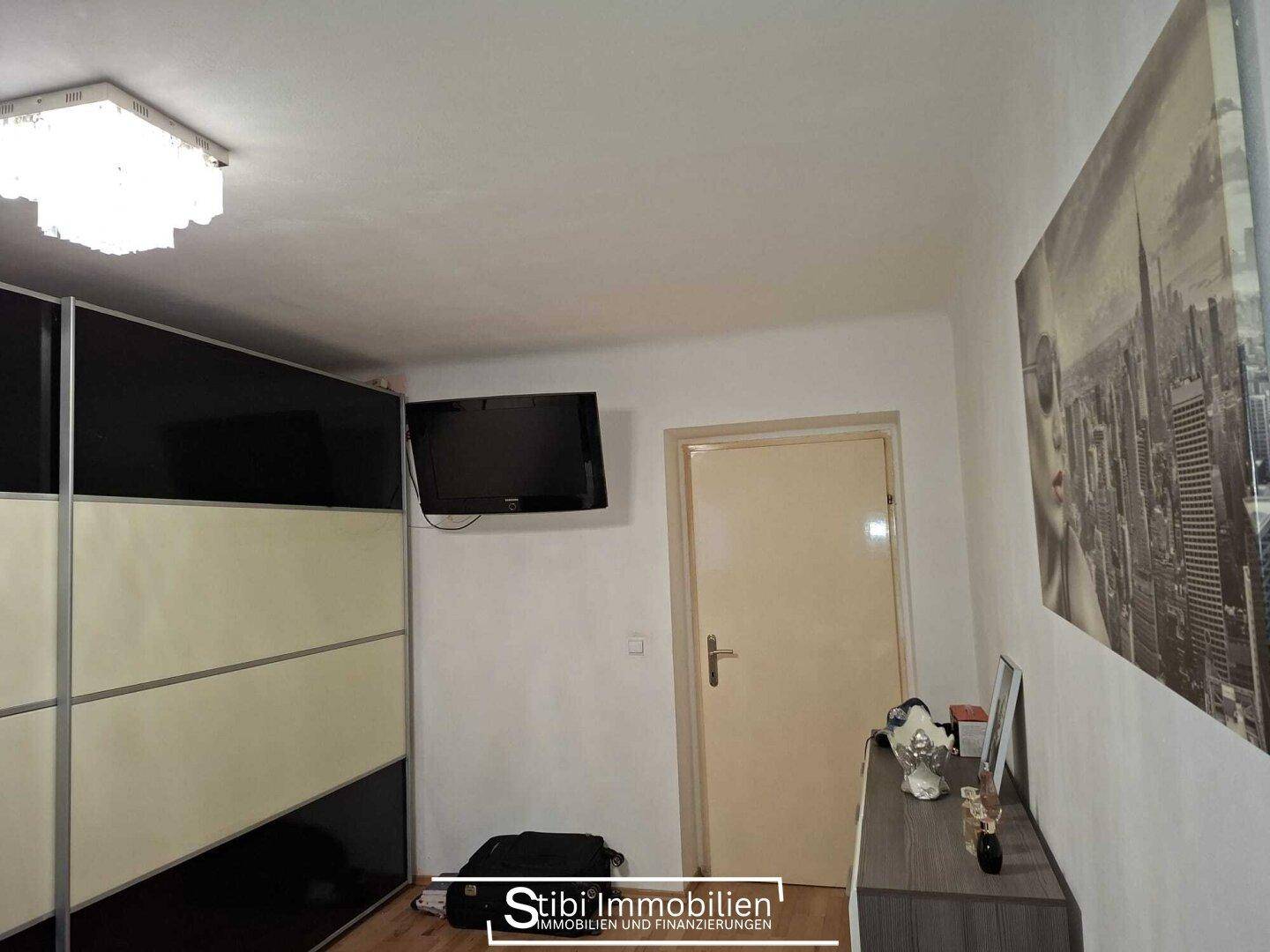 Schlafzimmer mit Schiebetürenschrank, Fernseher an der Wand und hellem Licht.
