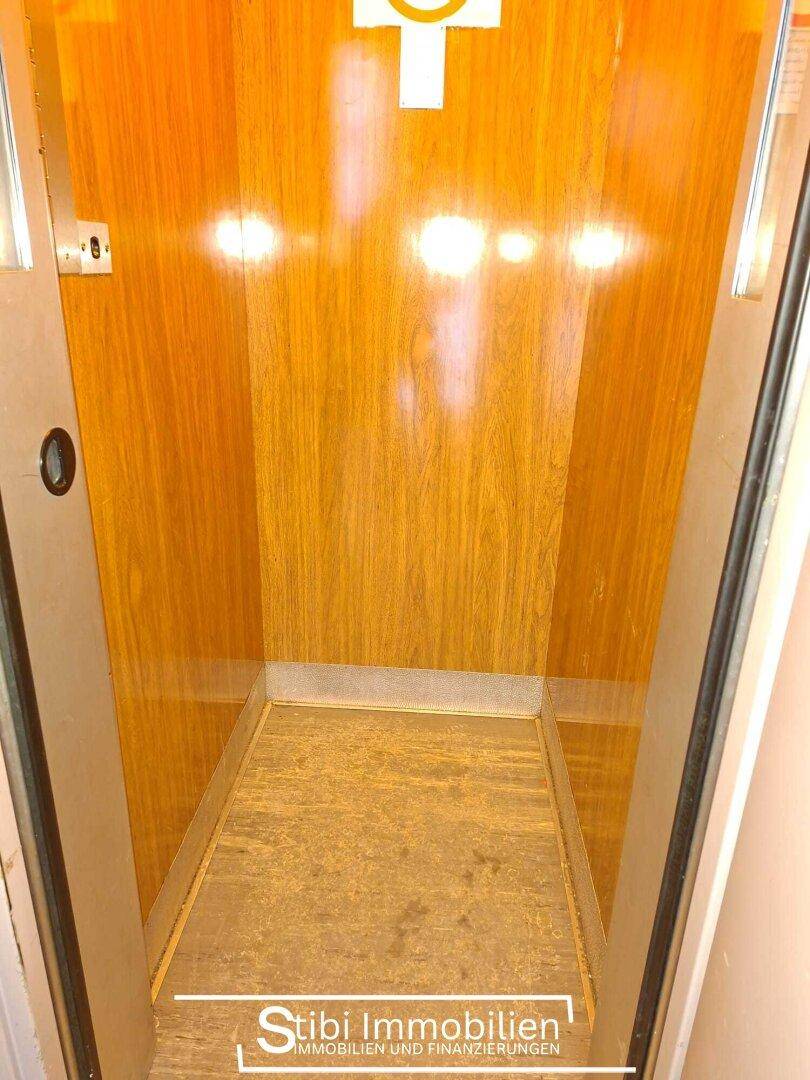 Innenansicht eines Aufzugs mit Holzwänden und hellem Boden.