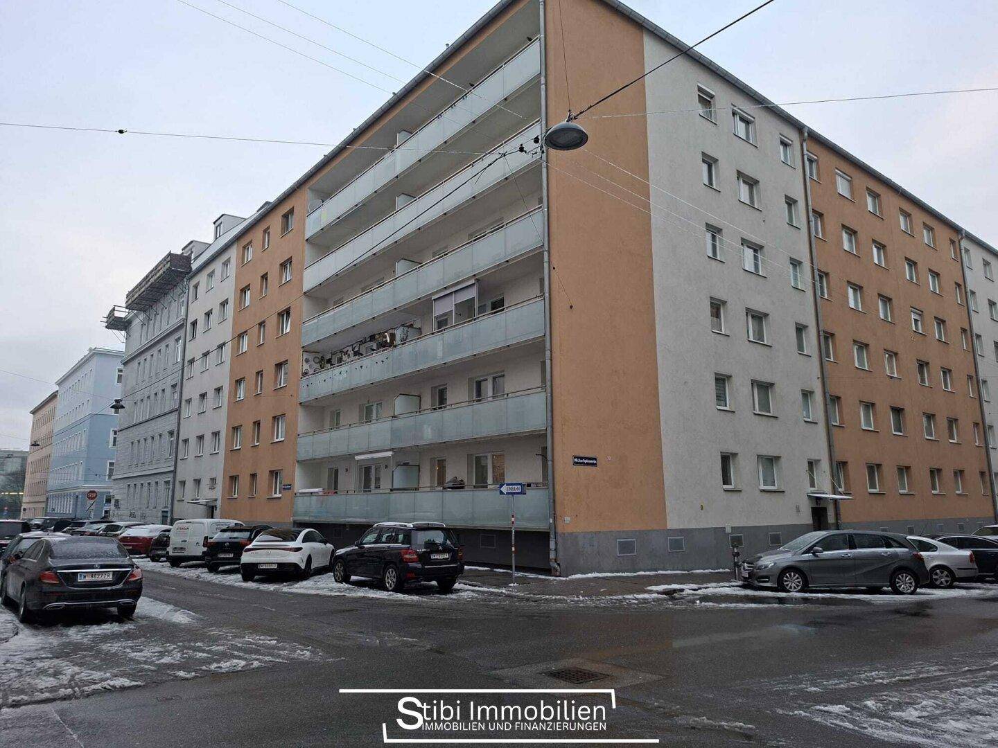 Mehrfamilienhaus mit Balkonen und parkenden Autos auf der Straße im Winter.