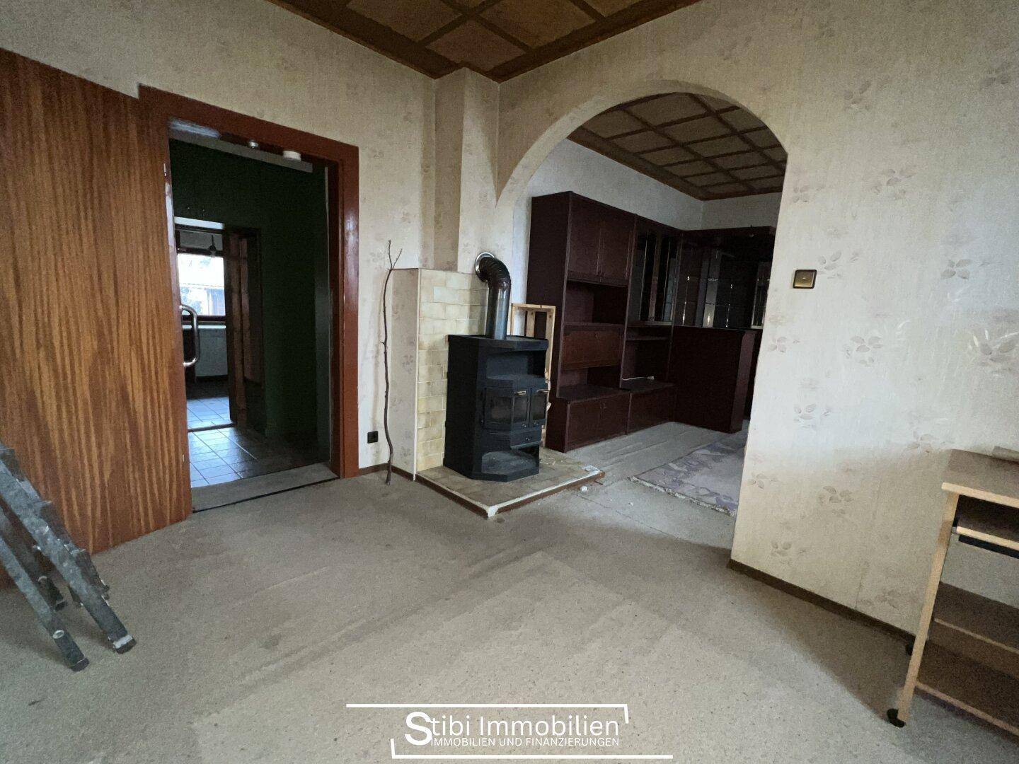 Geräumiges Wohnzimmer mit Holzofen, Teppichboden und Durchgang zu weiteren Räumen.