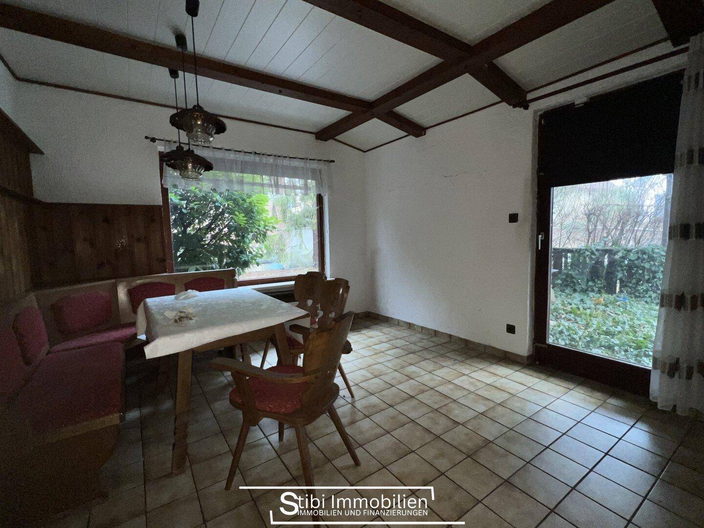 Rustikaler Essbereich mit Holzbalkendecke, Fliesenboden und Blick in den Garten.