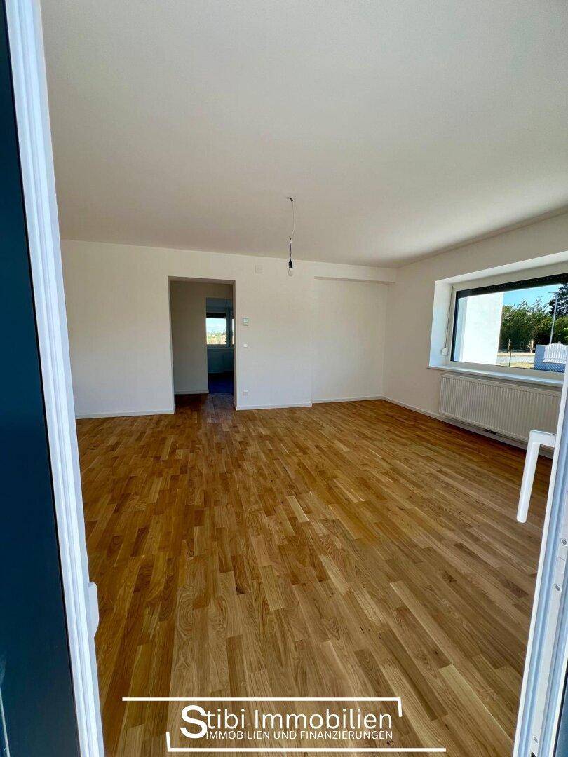 Helles, leeres Wohnzimmer mit neuem Holzparkettboden und weiß gestrichenen Wänden.