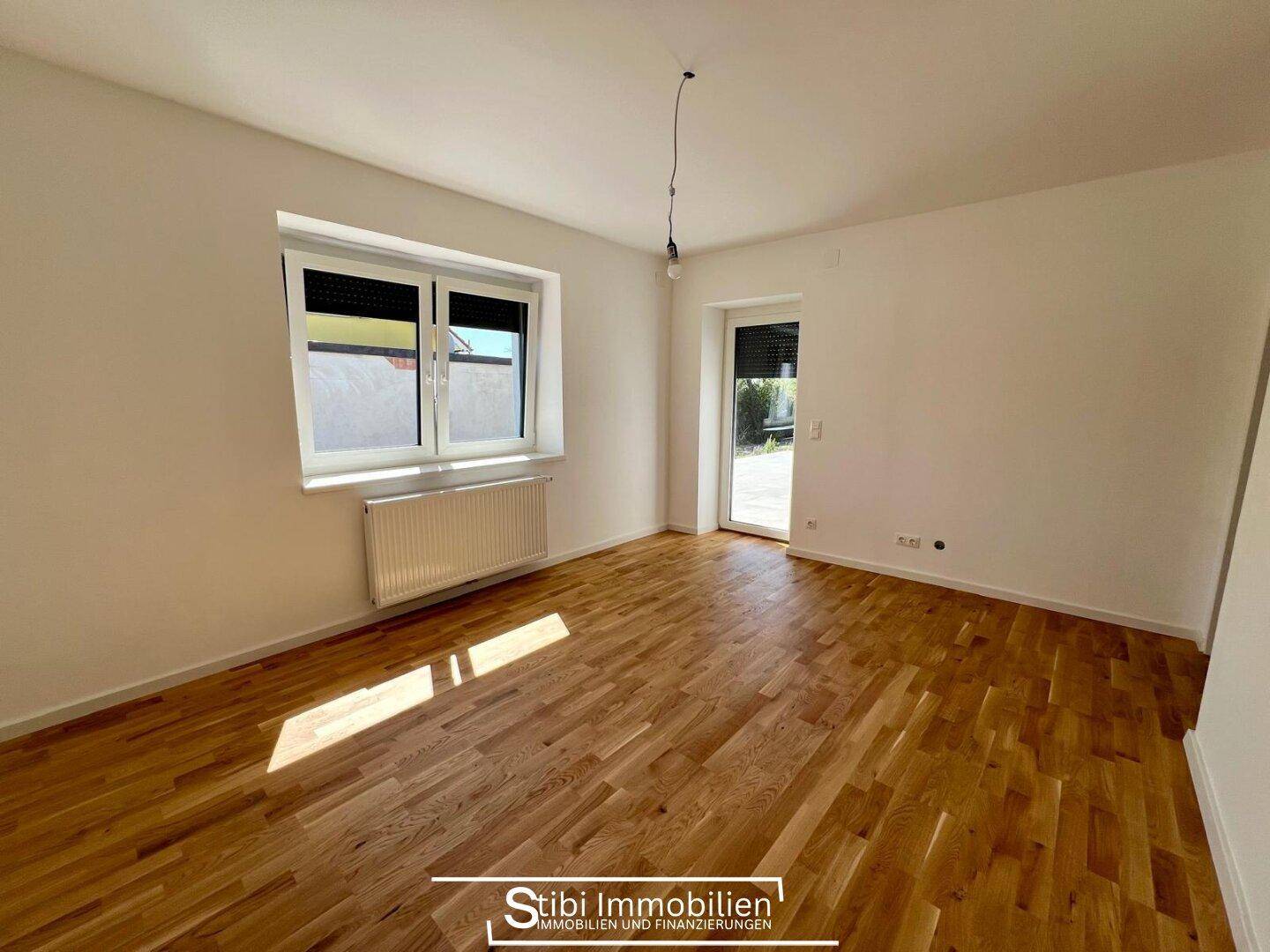 Helles Schlafzimmer mit Holzboden, Fenster und Zugang zu einem Außenbereich.